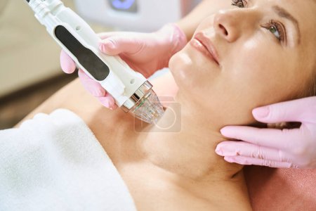 Photo for Close up of cropped female cosmetologist doing microneedle rf lifting of neck skin with IPL photorejuvenation device of adult caucasian woman in blurred beauty salon. Body skin care and rejuvenation - Royalty Free Image
