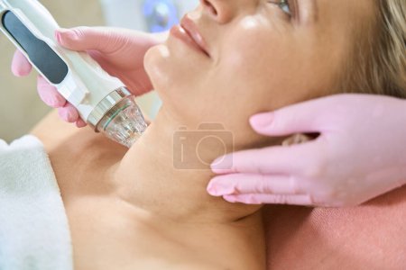 Photo for Partial image of female beautician doing microneedle rf lifting of neck skin with IPL photorejuvenation device of obscure face adult woman in blurred beauty salon. Body skin care and rejuvenation - Royalty Free Image