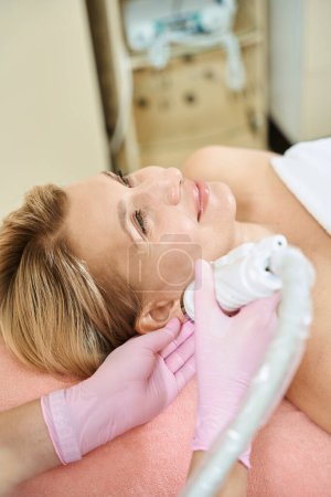 Photo for Partial female beautician doing microneedle rf lifting of ear skin with IPL photorejuvenation device of smiling adult european woman in blurred beauty salon. Concept of body skin care and rejuvenation - Royalty Free Image