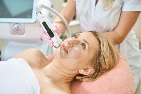 Photo for Partial female beautician doing microneedle rf lifting of skin with IPL photorejuvenation device of adult european woman in blurred beauty salon. Concept of body skin care and rejuvenation - Royalty Free Image