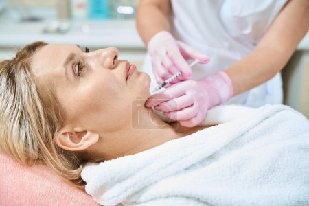 Photo for Side view of partial female cosmetologist doing face beauty injection with syringe of adult caucasian woman in blurred beauty salon. Face skin care, lifting and rejuvenation - Royalty Free Image