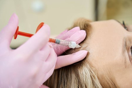Photo for Close up cropped view of female cosmetologist doing forehead beauty injection with syringe of woman in blurred beauty salon. Face skin care, lifting and rejuvenation - Royalty Free Image
