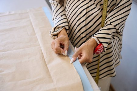 Téléchargez les photos : Femme dans un atelier épingle un motif à tissu, elle travaille à la table de coupe - en image libre de droit