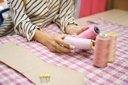 Téléchargez les photos : Artisanat dans l'atelier sélectionne des fils pour le tissu, elle travaille à la table de coupe - en image libre de droit