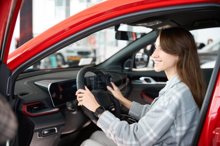 Photo for Happy young woman sitting inside her new car in dealership buying automobile in auto salon - Royalty Free Image