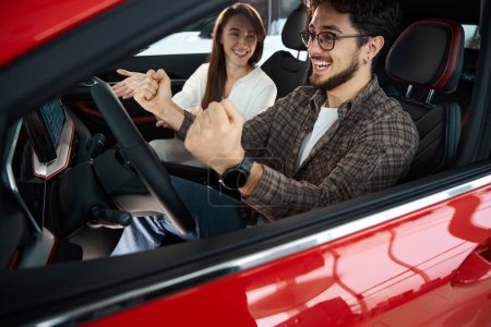 Téléchargez les photos : Heureux homme et femme assis dans une nouvelle auto célébrant l'achat d'une nouvelle voiture chez le concessionnaire - en image libre de droit