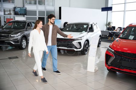 Photo for Full length of man and woman choosing car in auto salon thinking about automobile model and color - Royalty Free Image