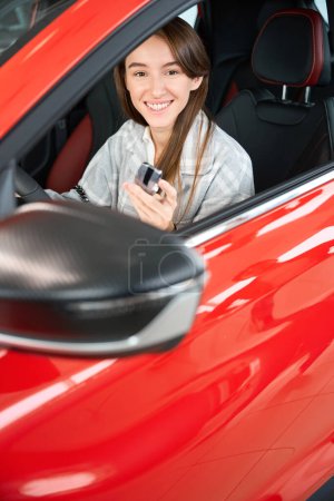 Foto de Mujer feliz conductor mostrando las llaves del coche mientras está sentado en su nuevo automóvil en la concesionaria - Imagen libre de derechos