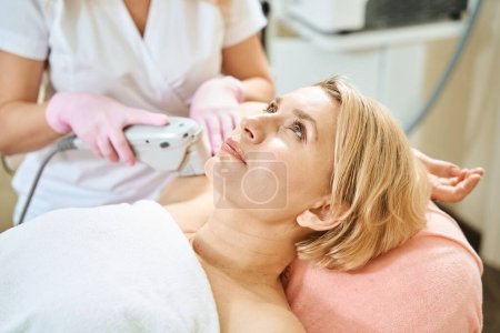 Photo for Partial female beautician doing laser depilation with laser hair removal machine of hand of adult blonde caucasian woman in blurred beauty salon. Concept of body skin care - Royalty Free Image