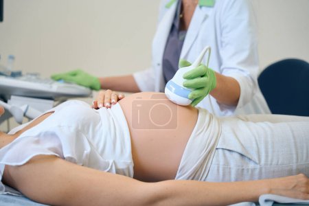 Téléchargez les photos : Image recadrée d'une gynécologue pratiquant une échographie chez une patiente enceinte en clinique. Concept d'examen de grossesse - en image libre de droit