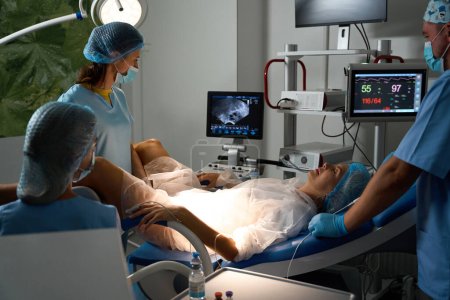 Téléchargez les photos : Le personnel de l'hôpital qui examine le moniteur pendant l'échographie de patiente enceinte sur le canapé médical avant l'accouchement en clinique de reproduction. Concept de grossesse et de maternité - en image libre de droit