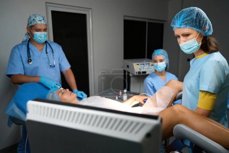 Photo for Focused hospital staff looking at monitor during doing ultrasound examination to pregnant female patient before childbirth in reproductive clinic. Concept of pregnancy and maternity - Royalty Free Image