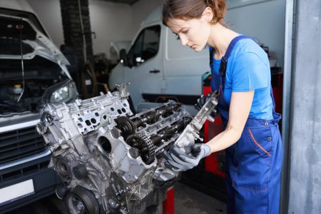 Foto de Mujer profesionalmente repara un motor de coche en un taller de reparación de automóviles, el maestro trabaja en guantes de protección y monos - Imagen libre de derechos