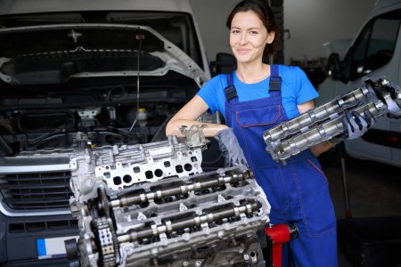 Woman holds a part of a modern car in her hands, the master works in protective gloves and overalls