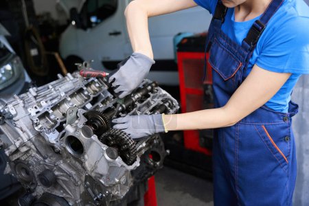 Téléchargez les photos : Mécanicien automobile répare le moteur d'une voiture moderne, une femme travaille dans des gants de protection et salopettes - en image libre de droit