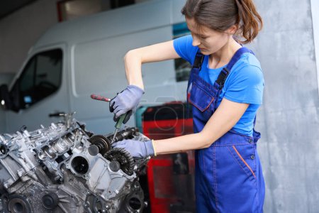 Foto de Joven mecánico de automóviles repara el motor de un coche moderno, una mujer trabaja en guantes de protección y monos - Imagen libre de derechos