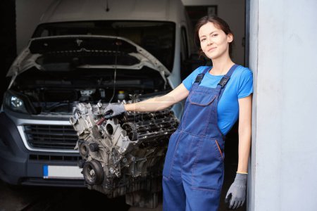 Téléchargez les photos : Femme mécanicien automobile sur le lieu de travail dans l'atelier près de la voiture et du moteur - en image libre de droit