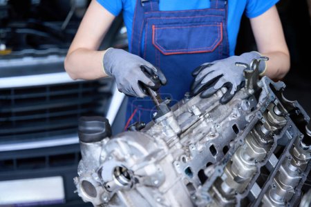 Téléchargez les photos : Femme mécanicien automobile sur le lieu de travail répare un moteur, elle utilise un outil spécial - en image libre de droit