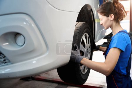 Téléchargez les photos : Femme mécanicien automobile inspecte la roue avant d'une voiture, la voiture est sur un ascenseur automatique - en image libre de droit