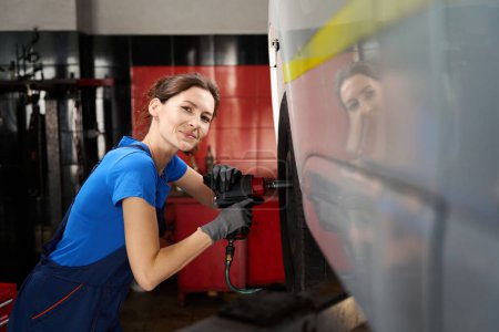 Photo for Female removes a wheel from a car on a car lift, a specialist uses a pneumatic wrench - Royalty Free Image