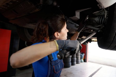 Téléchargez les photos : Femme mécanicien automobile inspecte la carrosserie d'une voiture dans un atelier de réparation automobile, la femme utilise un outil spécial - en image libre de droit