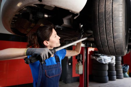 Photo for Auto mechanic specialist inspects car raised on a lift in a car repair shop, a woman uses a special tool - Royalty Free Image