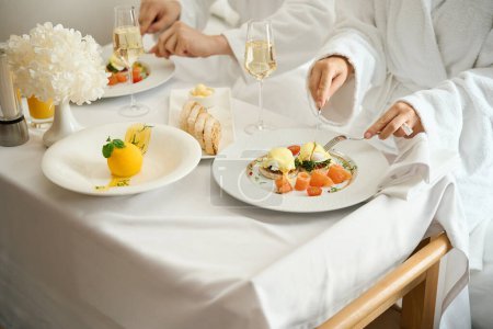 Téléchargez les photos : Les clients de l'hôtel prennent le petit déjeuner en peignoirs, le petit déjeuner est servi dans la chambre - en image libre de droit