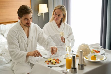Foto de Hermosa pareja desayunando en la habitación del hotel, mujer disfrutando del champán - Imagen libre de derechos
