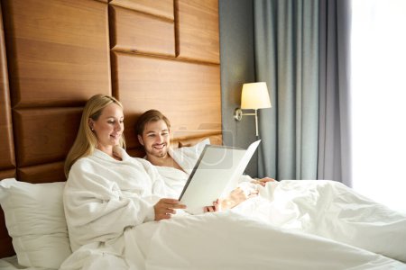 Foto de Despertó recién casados estudiar el menú en la cama, la pareja elige el desayuno en la habitación - Imagen libre de derechos