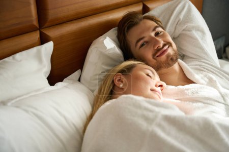 Téléchargez les photos : Jeune femme somnolant sur l'épaule d'un homme heureux, couple relaxant sur un grand lit - en image libre de droit