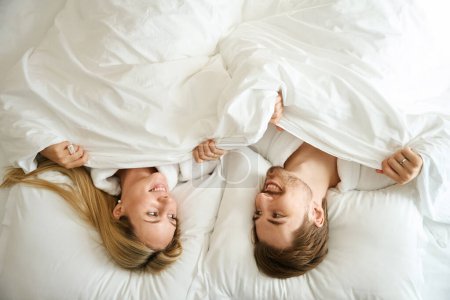 Téléchargez les photos : Les jeunes mariés sont couchés dans une chambre d'hôtel, ils se regardent avec amour - en image libre de droit