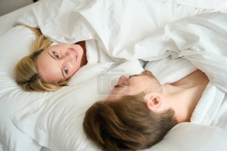 Foto de El hombre y una mujer están acostados en la cama en una habitación de hotel, llevan túnicas de felpa acogedoras. - Imagen libre de derechos