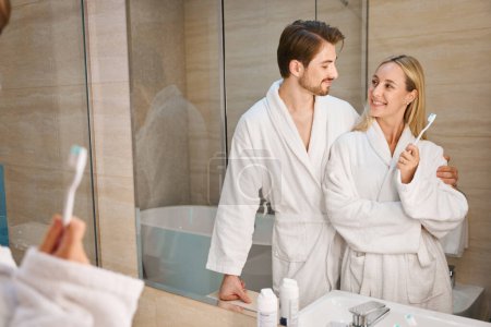 Photo for Guy with a girlfriend in the bathroom doing their morning routine, a couple in cozy terry robes - Royalty Free Image