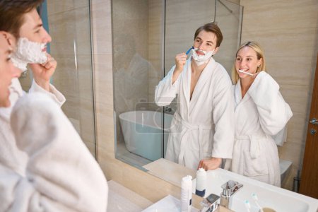 Téléchargez les photos : Femme blonde avec petit ami dans la salle de bain faisant la routine du matin, homme rasage, femme brossant les dents - en image libre de droit