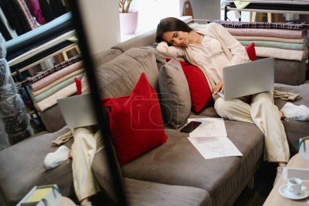 Foto de Mujer embarazada está dormitando sobre almohadas suaves, ella tiene un ordenador portátil en sus manos - Imagen libre de derechos