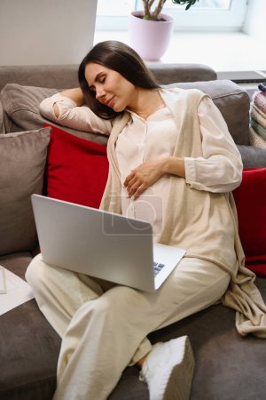 Téléchargez les photos : Femme fatiguée sommeille sur des oreillers souples, elle a un ordinateur portable dans ses mains - en image libre de droit