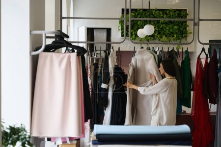 Téléchargez les photos : Femme regardant une collection de vêtements dans un studio de créateurs, femme dans des vêtements décontractés confortables - en image libre de droit