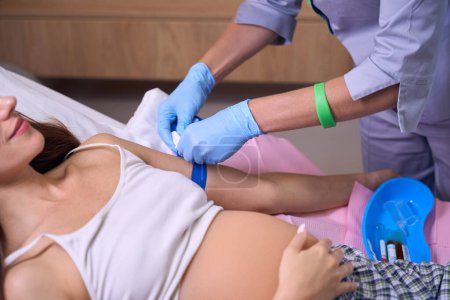 Photo for Cropped image of female nurse preparing hand of young pregnant woman to injection on medical bed in hospital. Concept of pregnancy and maternity - Royalty Free Image