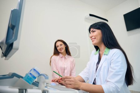 Photo for Smiling adult european female gynecologist and young caucasian pregnant woman watching ultrasound results on screen in clinic. Concept of pregnancy examination - Royalty Free Image