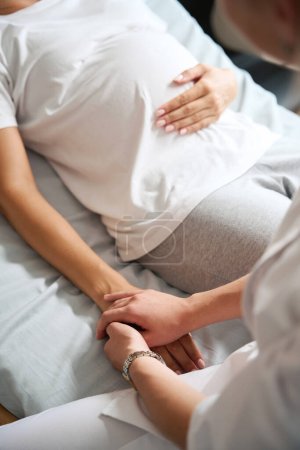 Foto de Imagen parcial de una enfermera cogida de la mano de una mujer embarazada en la cama médica en el hospital de maternidad - Imagen libre de derechos