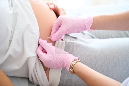 Foto de Imagen recortada del médico que administra la inyección con jeringa en el vientre embarazada de una paciente en la clínica de maternidad - Imagen libre de derechos