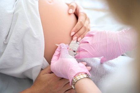 Foto de Imagen parcial de la enfermera que administra la inyección con jeringa en el vientre embarazada de una paciente en la clínica de maternidad - Imagen libre de derechos