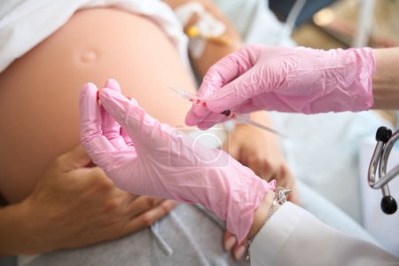 Foto de Imagen recortada de las manos del médico en guantes de látex que preparan la jeringa para inyección en el vientre embarazada de una paciente femenina borrosa en la clínica de maternidad - Imagen libre de derechos