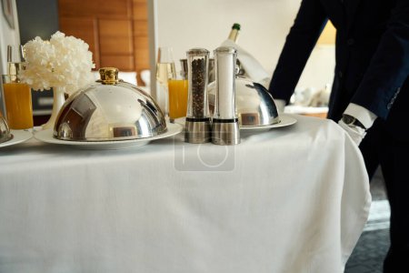 Photo for Hotel staff delivers a champagne meal to your room, the food is covered in glittering cloche - Royalty Free Image