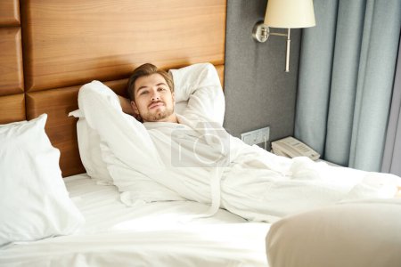 Foto de Huéspedes del hotel en un albornoz descansa sobre una cama grande, el hombre tiene una barba pequeña - Imagen libre de derechos