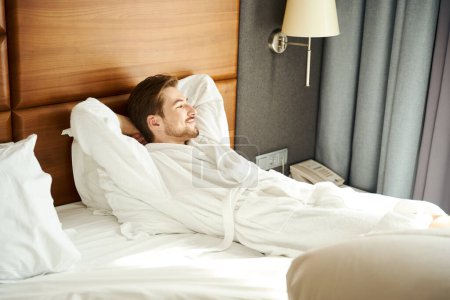 Foto de Joven descansando en una cama grande, hombre con un albornoz esponjoso - Imagen libre de derechos
