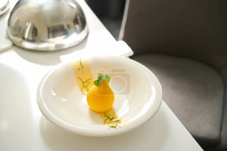 Foto de Exquisito postre se sirve con hojas de menta en plato blanco, tapa de cloche se encuentra junto a ella en la mesa de servir - Imagen libre de derechos