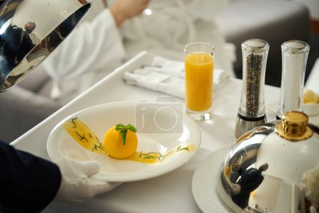 Téléchargez les photos : Serveur sert le petit déjeuner à un client de l'hôtel au lit, un homme portant des gants blancs - en image libre de droit
