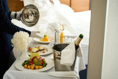 Téléchargez les photos : Servant le petit déjeuner dans la chambre avec champagne sur une table de service, serveur en gants blancs - en image libre de droit