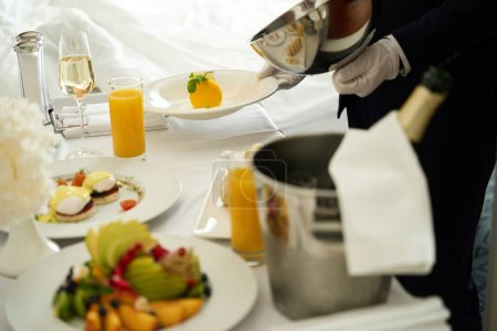 Foto de El camarero sirve el desayuno en la habitación, un hombre con guantes blancos - Imagen libre de derechos